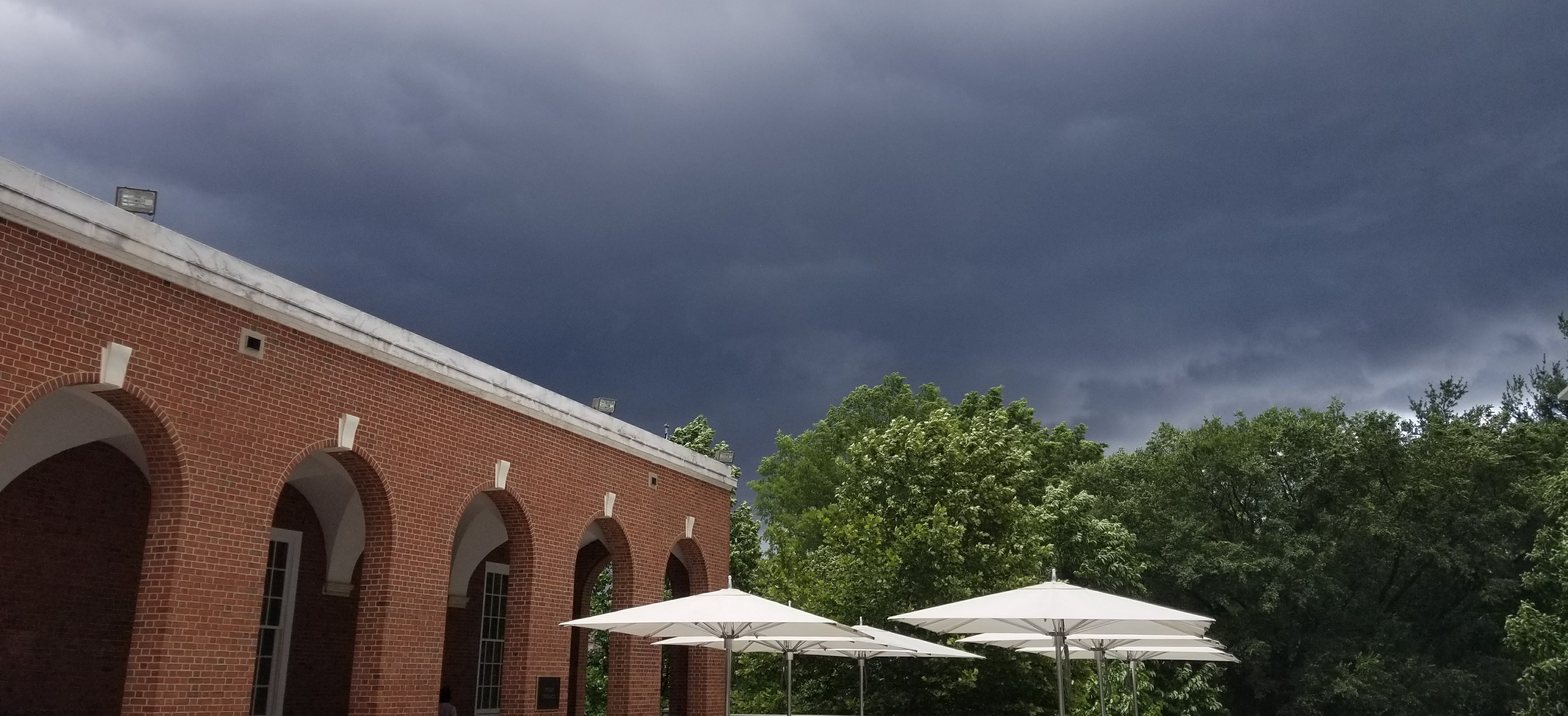 Brick archway and white umbrellas overshadowed by clouds.